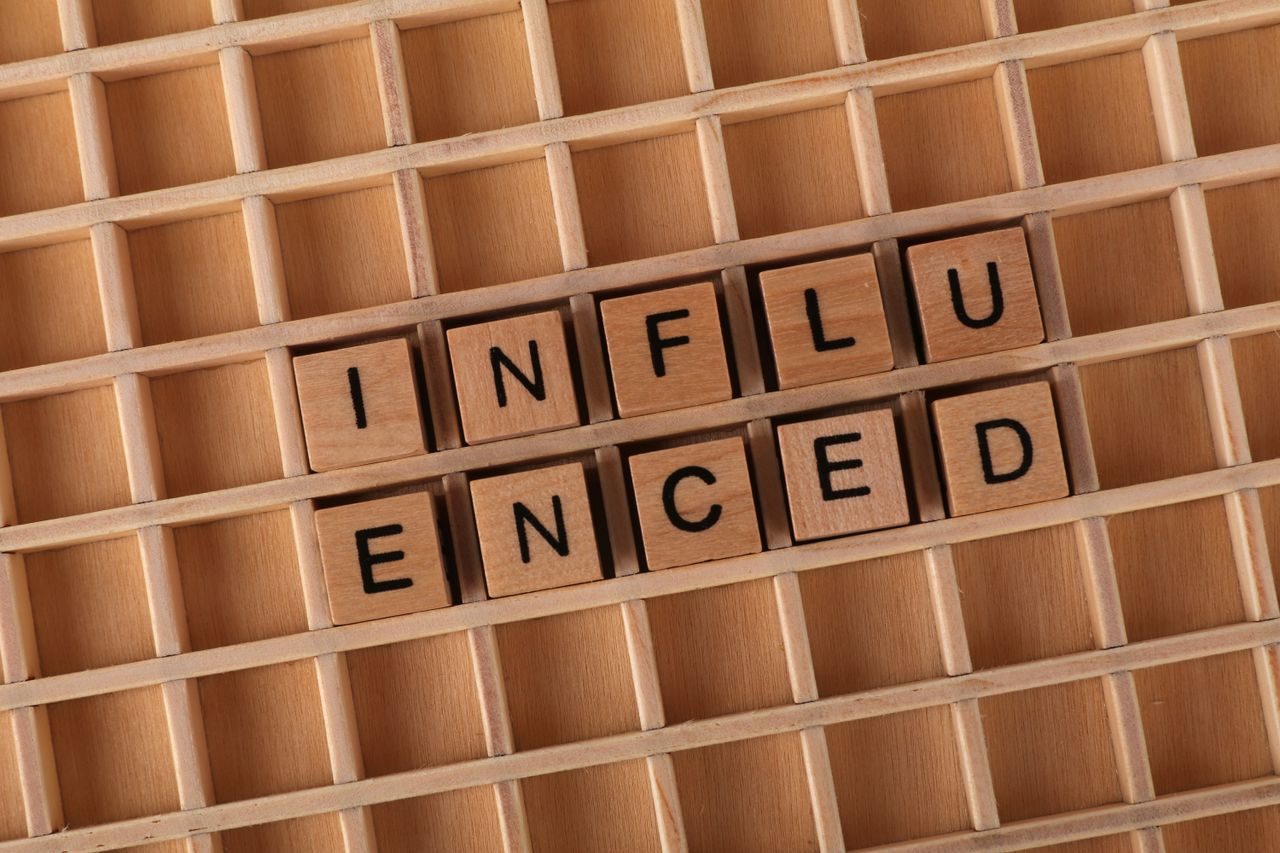 Des tuiles en bois de Scrabble formant le mot Influenced sur un fond de grille en bois.